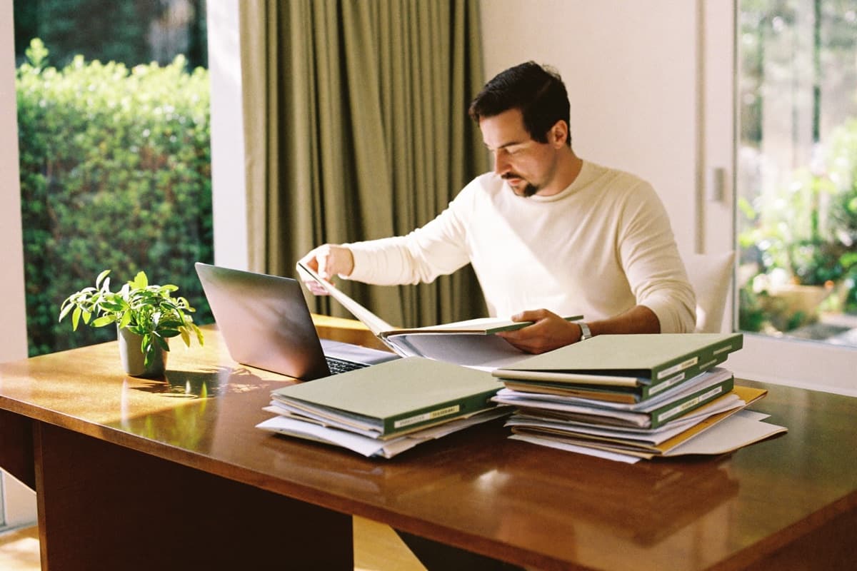A grant writer reviewing documents beside a laptop at a sunlit desk.